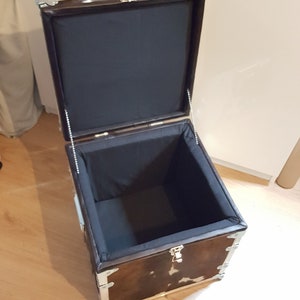 May include: A brown and white cowhide storage trunk with silver metal accents and a black fabric lining. The trunk is open and the lid is propped up.