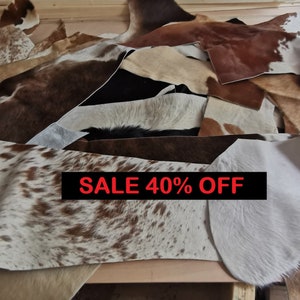 May include: A selection of cowhide leather pieces in various colours and patterns, including white, brown, and black. The leather pieces are laid out on a wooden surface. The text "SALE 40% OFF" is displayed in red lettering.