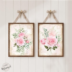 May include: Two rectangular wall art prints in dark wood frames, each featuring a bouquet of pink roses and green foliage on a pale, patterned background. Each print is suspended by a beige ribbon tied in a bow at the top of the frame.