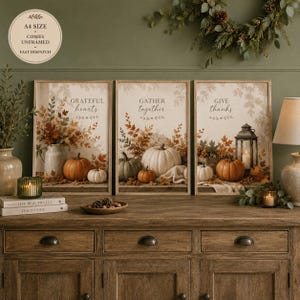 May include: A set of three A4 size unframed wall art prints featuring autumn themes. The prints display pumpkins, fall foliage, and lanterns with the text "GRATEFUL hearts", "GATHER together", and "GIVE thanks" in a neutral colour palette.