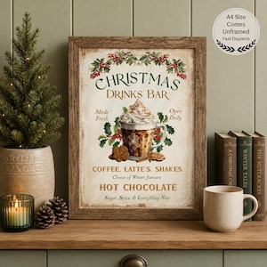 Op de afbeelding: Een ingelijste kunstprint getiteld Christmas Drinks Bar met een centrale illustratie van een latte met slagroom, hulst en koekjes. De tekst luidt Made Fresh, Open Daily, Coffee, Latte, Shakes, Hot Chocolate, Sugar, Spice, & Everything Nice.
