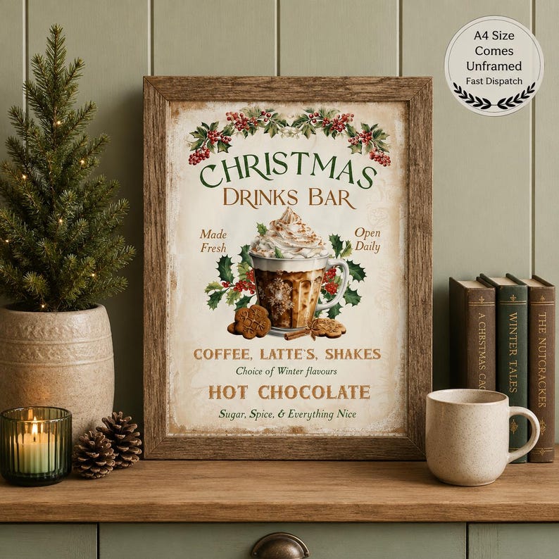Op de afbeelding: Een ingelijste kunstprint getiteld Christmas Drinks Bar met een centrale illustratie van een latte met slagroom, hulst en koekjes. De tekst luidt Made Fresh, Open Daily, Coffee, Latte, Shakes, Hot Chocolate, Sugar, Spice, & Everything Nice.