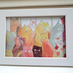 Peut inclure: Une impression encadrée à l'aquarelle représentant un groupe de chats de différentes couleurs, notamment orange, jaune, marron et rose. Les chats ont des motifs et des expressions variés. Le cadre est blanc.