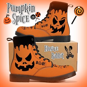 Puede incluir: Botas naranjas con temática de Halloween con cordones y suelas negros. Las botas presentan un diseño de cara de calabaza, la palabra "BOO!" y el texto "Pumpkin Spice". Las botas están sobre una caja de cartón con el texto "Elusive Rabbit".
