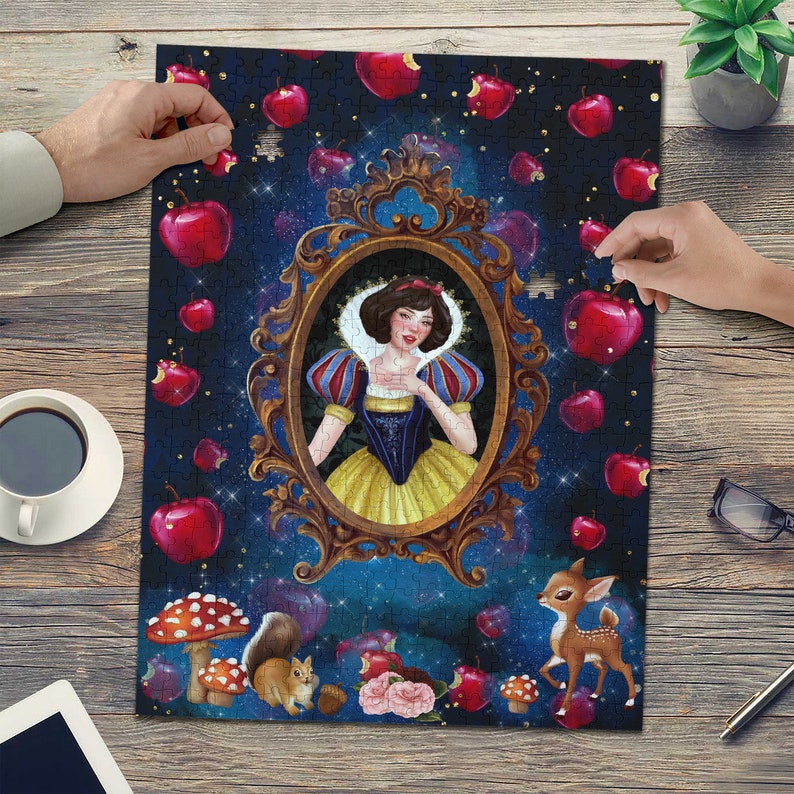 May include: A jigsaw puzzle featuring a whimsical illustration of Snow White, surrounded by red apples and a deer. The princess is framed in a gold ornate mirror, set against a dark blue starry background.