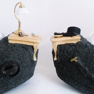 May include: Two miniature wooden tables with black fabric bases. One table has a small lamp with a white shade and the other has a black top hat.