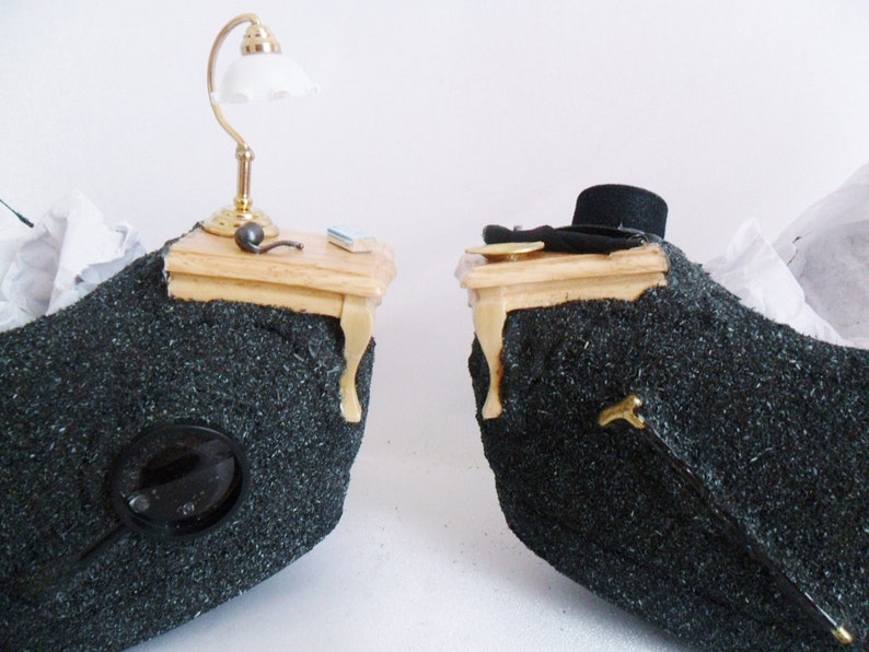 May include: Two miniature wooden tables with black fabric bases. One table has a small lamp with a white shade and the other has a black top hat.