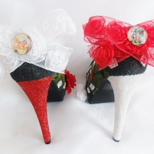 May include: A pair of high-heeled shoes decorated with red and white bows. The shoes are black with red glitter on the heels and white glitter on the other shoe. The bows are made of tulle and have a small button with a picture of a rabbit on them.