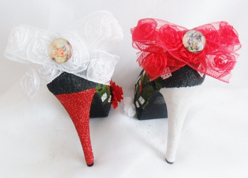 May include: A pair of high-heeled shoes decorated with red and white bows. The shoes are black with red glitter on the heels and white glitter on the other shoe. The bows are made of tulle and have a small button with a picture of a rabbit on them.
