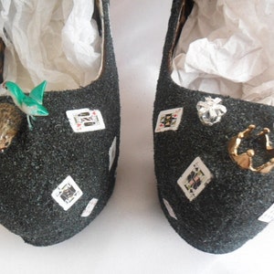 May include: A pair of black glitter high-heeled shoes decorated with playing cards, a crown, and other embellishments.