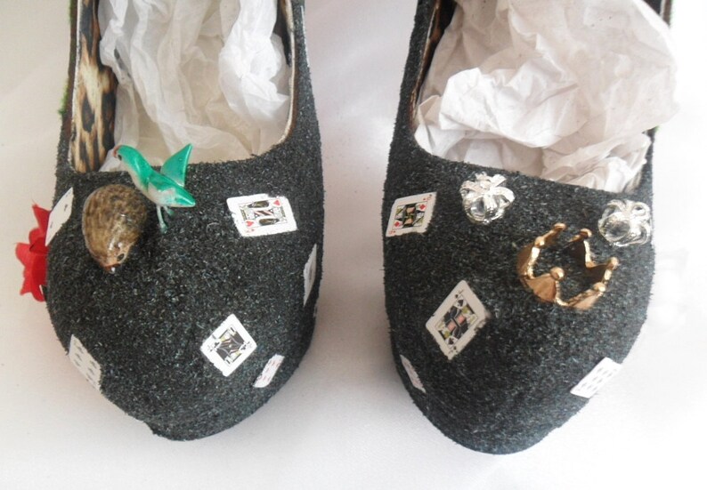 May include: A pair of black glitter high-heeled shoes decorated with playing cards, a crown, and other embellishments.
