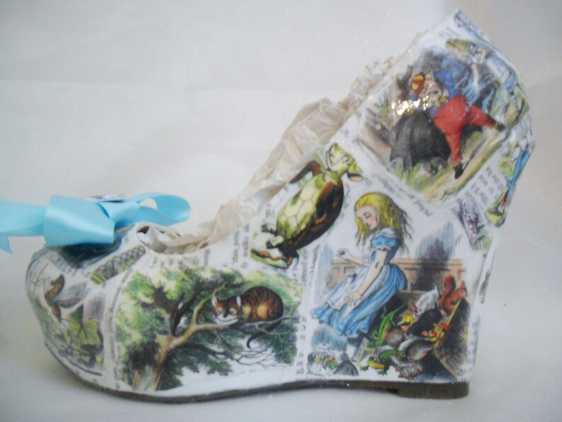 May include: White wedge shoe with a colorful Alice in Wonderland print featuring characters like the Cheshire Cat, the Mad Hatter, and the Queen of Hearts.