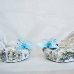 May include: A pair of white wedge shoes with a blue bow on each shoe. The shoes are covered in a print of a children's book illustration.
