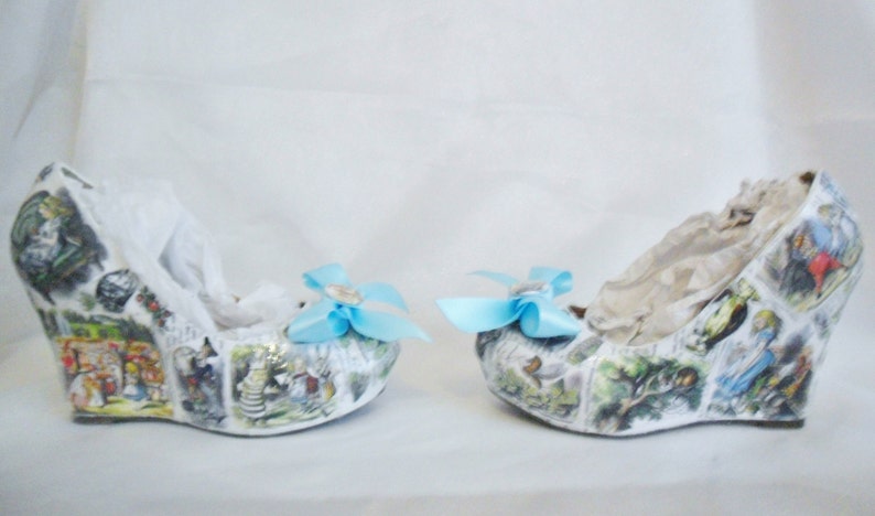 May include: A pair of white wedge shoes with a blue bow on each shoe. The shoes are covered in a print of a children's book illustration.