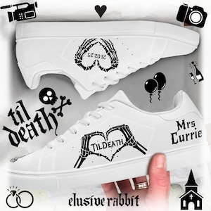 May include: White canvas sneakers with black skeleton hand designs. One shoe says "Til Death" and the other says "Mrs. Currie" with a heart and the date "21.03.22".