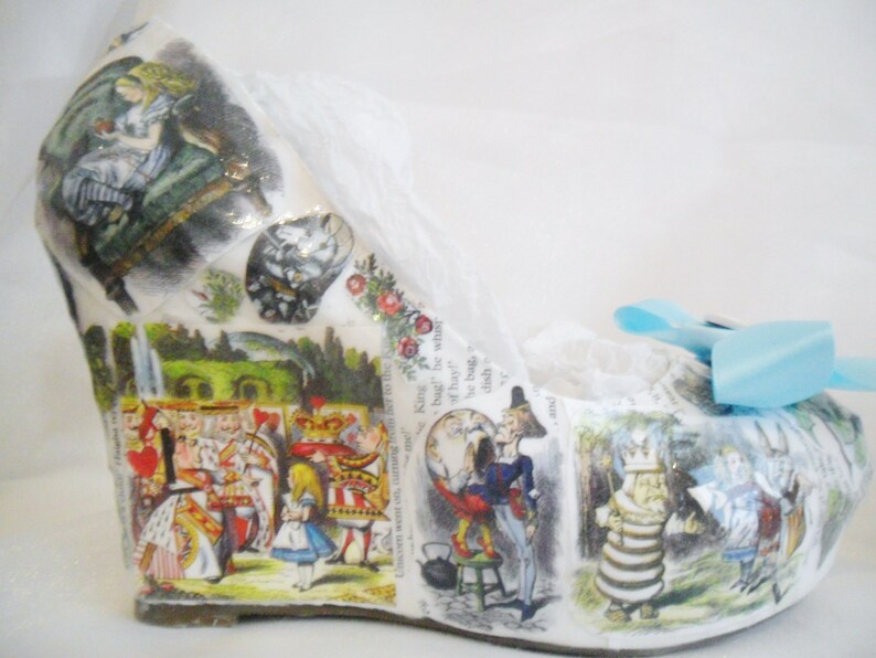 May include: White wedge shoe with a blue bow. The shoe is decorated with images from Alice in Wonderland, including Alice, the Queen of Hearts, and the Mad Hatter.