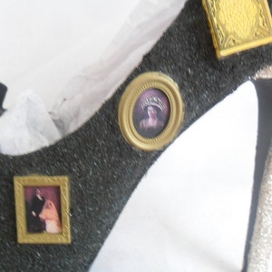 May include: A black high-heeled shoe with gold accents. The shoe is decorated with three small framed pictures. One picture features a woman in a crown, another picture features a couple, and the third picture features a decorative design.