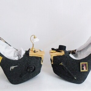 May include: A pair of black high-heeled shoes with glitter accents. Each shoe features a miniature desk with a lamp, a picture frame, and other decorative elements.