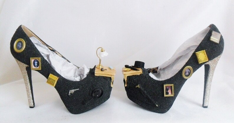 May include: A pair of black high-heeled shoes with glitter accents. Each shoe features a miniature desk with a lamp, a picture frame, and other decorative elements.