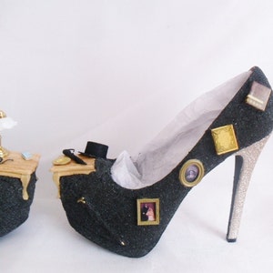 May include: A black high-heeled shoe with a glitter finish and gold accents. The shoe is decorated with miniature framed pictures and a small lamp on the side.