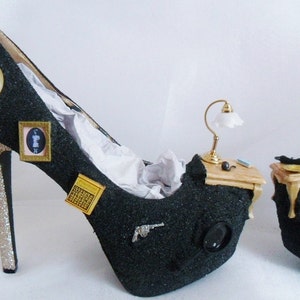 May include: A pair of black high-heeled shoes with gold glitter heels. The shoes are decorated with miniature furniture, a lamp, and other small objects.