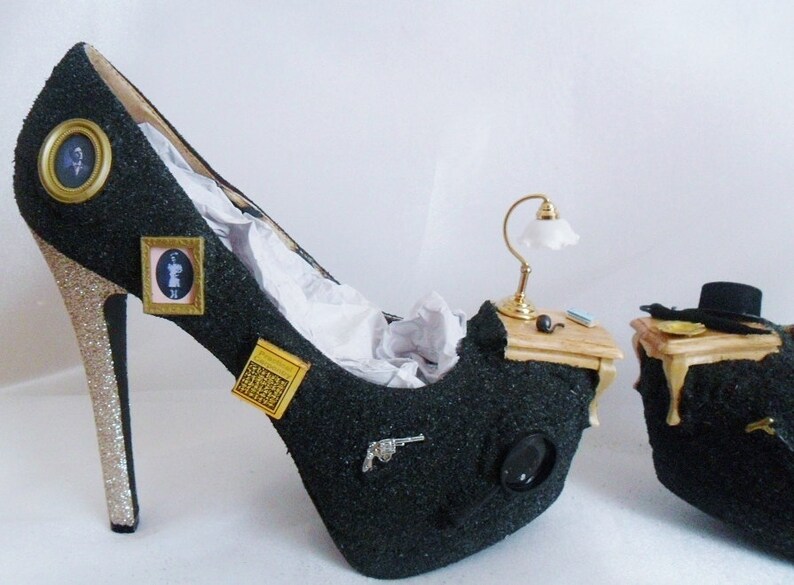 May include: A pair of black high-heeled shoes with gold glitter heels. The shoes are decorated with miniature furniture, a lamp, and other small objects.