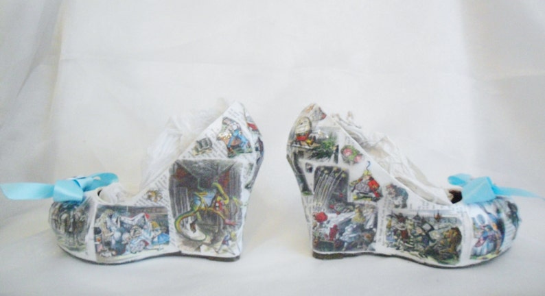 May include: A pair of white wedge shoes with a blue bow. The shoes are covered in a collage of images from a book, possibly Alice in Wonderland.