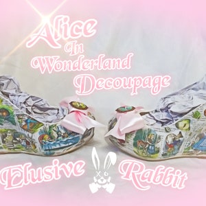 May include: A pair of white wedge shoes decorated with a decoupage design featuring scenes from Alice in Wonderland. The shoes have pink bows and the text "Alice in Wonderland Decoupage Elusive Rabbit" is printed on the background.