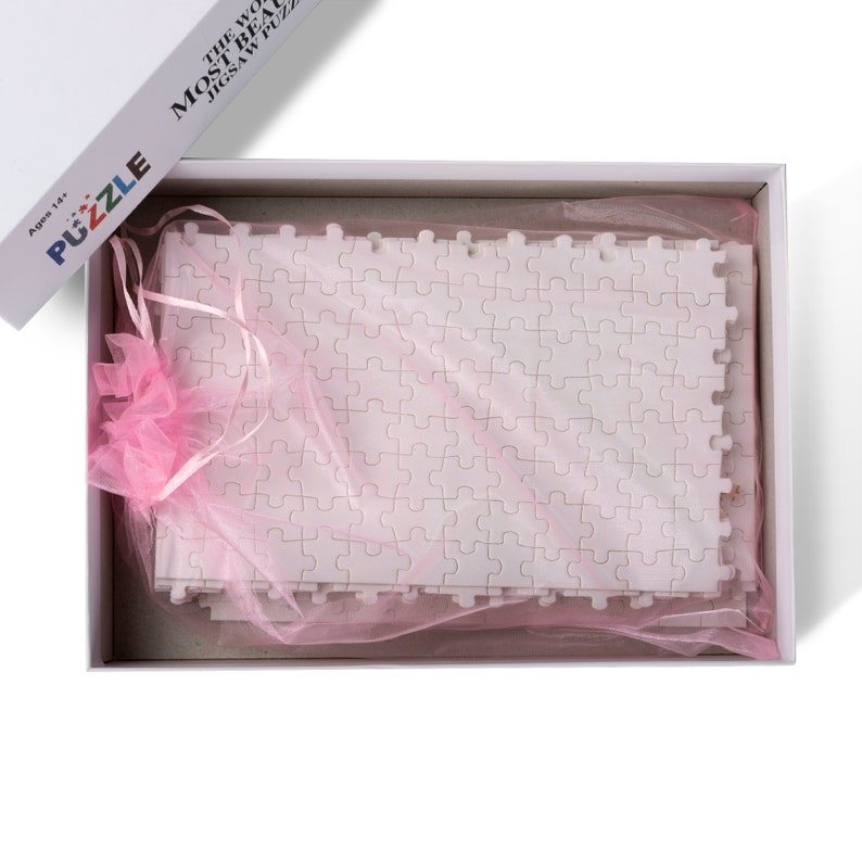 May include: A white jigsaw puzzle in a white box with a pink tulle bag. The box has the text "The World's Most Beautiful Jigsaw Puzzle" on the side.