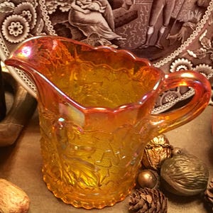 May include: A vintage amber glass pitcher with a textured leaf design. The pitcher has a iridescent finish and a wide, rounded spout.