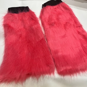 Puede incluir: Dos calentadores de piernas de color rosa peludo con bandas elásticas negras en la parte superior.