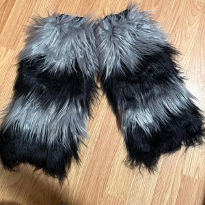 May include: A pair of black and silver faux fur leg warmers. The leg warmers are made of soft, fluffy fur and have a striped pattern.
