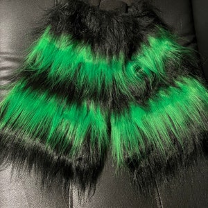 May include: A pair of faux fur leg warmers in black and green. The leg warmers have a striped pattern with alternating bands of black and bright green. The fur appears long and shaggy.