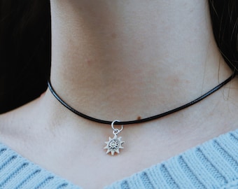 May include: A black choker necklace with a silver sun pendant. The pendant has a detailed design with a circle in the center.