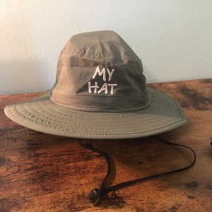 Pode incluir: Um chapéu de pescador verde com um design bordado branco que diz "MY HAT".