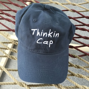 May include: A dark blue baseball cap with white embroidery that says "Thinkin Cap".