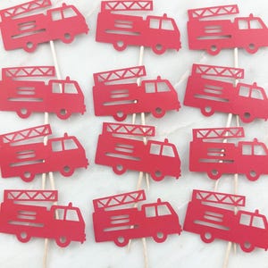 May include: Red fire truck cupcake toppers on wooden sticks. The toppers are cut from red cardstock and feature a ladder on top. These are perfect for a fire truck themed party.