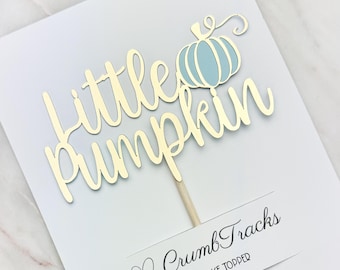 Op de afbeelding: Gouden glitter taarttopper met de woorden "little pumpkin" en een blauwe pompoen. De topper is op een witte achtergrond met een hartje en de woorden "Crumb Tracks Cake Topper".