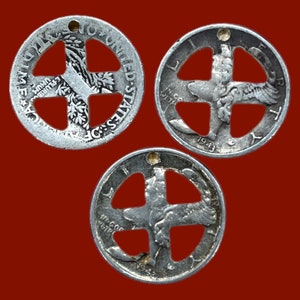 Op de afbeelding: Drie zilveren Amerikaanse halve dollar munten met een kruisvormig gat dat uit het midden is geknipt. De munten zijn uit 1943, 1942 en 1941.