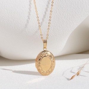 May include: A gold chain necklace with a gold oval locket pendant. The locket has a detailed floral design.