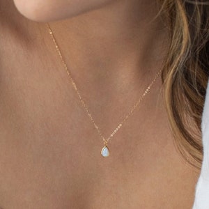 May include: A delicate gold chain necklace with a small teardrop-shaped opal pendant.