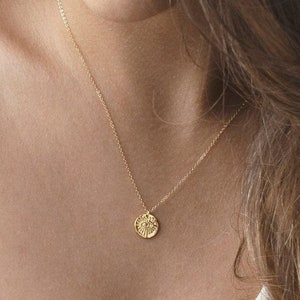 May include: A gold necklace with a small, round pendant. The pendant has a textured surface and appears to have a design on it.