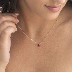 May include: A delicate gold chain necklace with a small, teardrop-shaped ruby pendant.