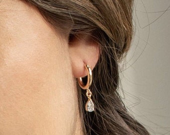 May include: Gold hoop earrings with a dangling teardrop-shaped crystal.