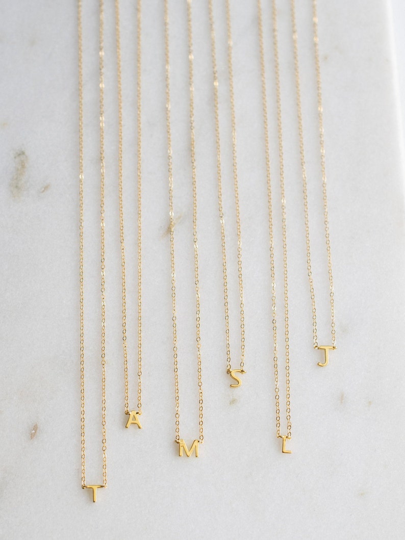 May include: A set of nine gold necklaces with small letter charms. The letters are T, A, M, L, S, and J.
