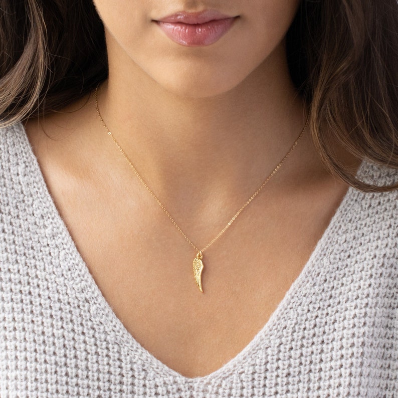 May include: A gold chain necklace with a delicate, textured, gold wing pendant.