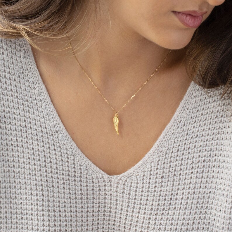 May include: A gold chain necklace with a delicate gold wing pendant.