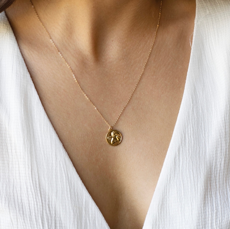 Może przedstawiać: Złoty naszyjnik z łańcuszkiem i małym okrągłym wisiorem z motywem anioła.