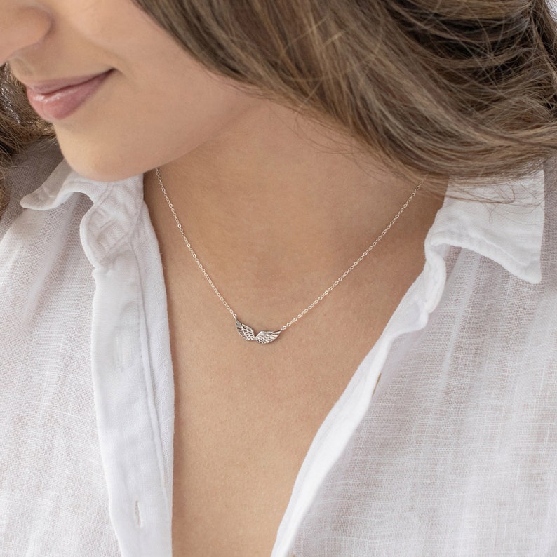 Pu&ograve; includere: Una collana d'argento con un delicato ciondolo a forma di ala. La collana &egrave; indossata da un modello che indossa una camicia bianca.