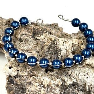May include: A dark blue pearl bracelet with silver wire wrapping. The bracelet is made with round pearls and has a simple design.